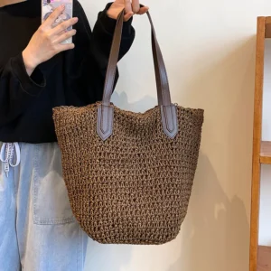 Premium handmade rattan woven summer beach bag in deep brown with dark leather handles carried by a woman wearing a casual black top